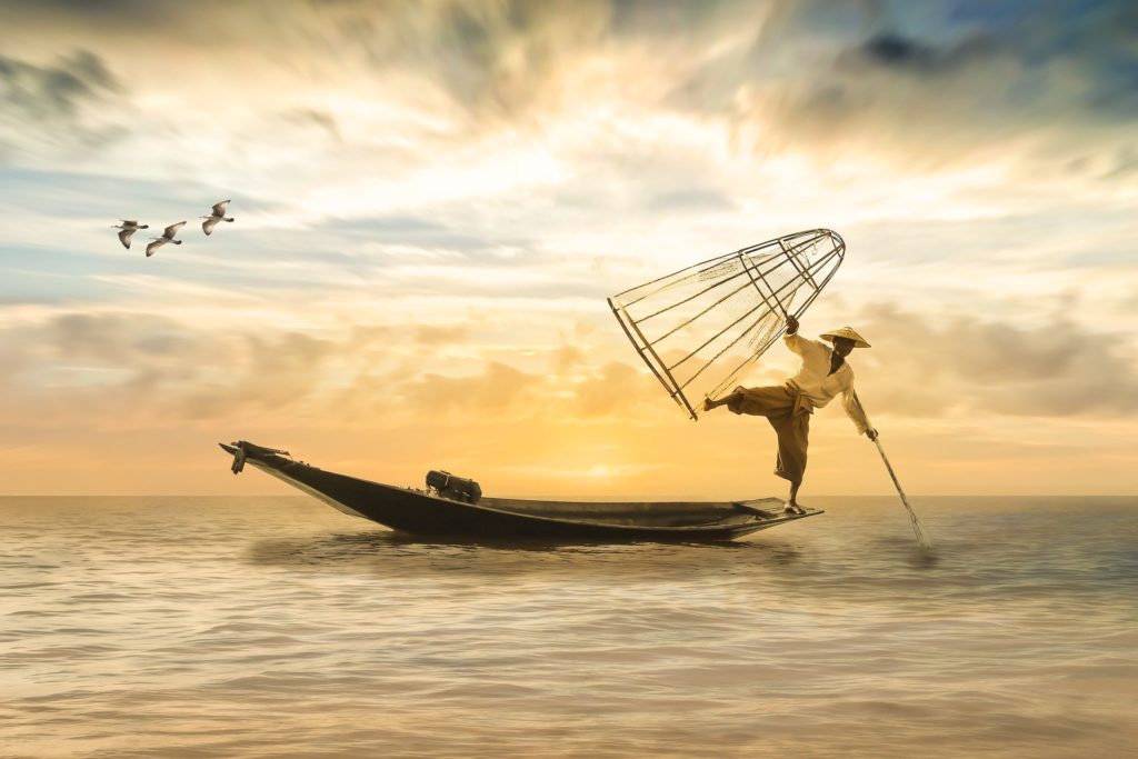 fisherman with basket balancing on a long boat with inspiring sunset